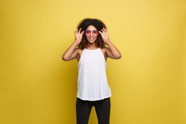 Photo gratuite belle femme afro-américaine attrayante avec des lunettes à la mode posant sur un fond de studio jaune. espace de copie.