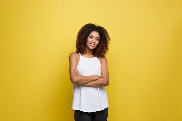 Belle femme afro-américaine attrayante posant jouer avec ses cheveux bouclés d&#39;afro. Fond d&#39;écran jaune. Espace de copie.