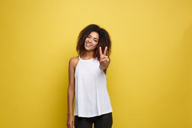 Belle femme afro-américaine attrayante posant jouer avec ses cheveux bouclés d&#39;afro. Fond d&#39;écran jaune. Espace de copie.