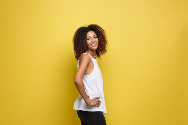 Belle femme afro-américaine attrayante posant jouer avec ses cheveux bouclés d&#39;afro. Fond d&#39;écran jaune. Espace de copie.