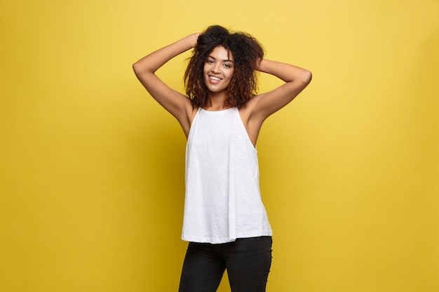 Belle femme afro-américaine attrayante posant jouer avec ses cheveux bouclés d&#39;afro. Fond d&#39;écran jaune. Espace de copie.