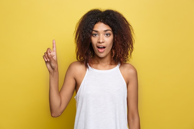 Belle femme afro-américaine attrayante posant jouer avec ses cheveux bouclés d&#39;afro. Fond d&#39;écran jaune. Espace de copie.