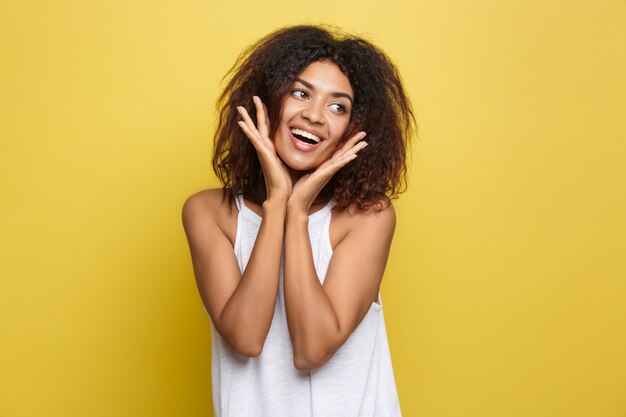 Belle femme afro-américaine attrayante posant jouer avec ses cheveux bouclés d&#39;afro. Fond d&#39;écran jaune. Espace de copie.