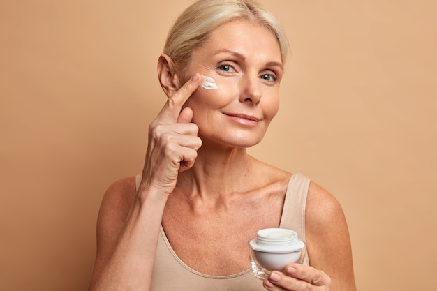 Belle femme d'âge moyen applique une crème anti-vieillissement sur le visage subit des soins de beauté se soucie de la peau