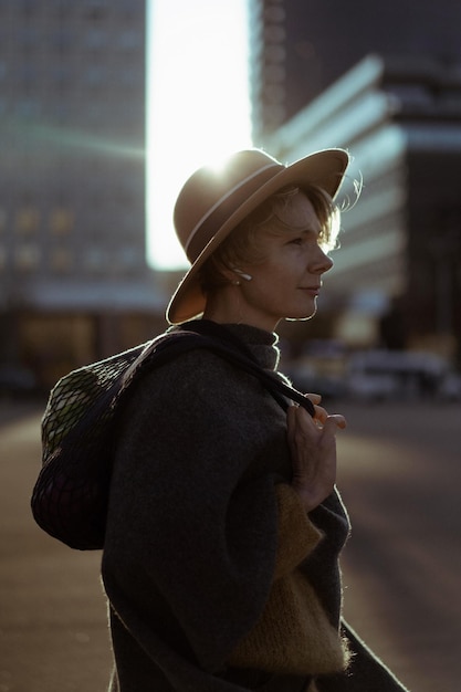 Belle femme d'âge moyen dans un chapeau avec une coupe de cheveux courte au centre d'une grande ville. Portrait en gros plan, rétro-éclairage doux.