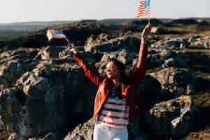 Photo gratuite belle femme agitant des drapeaux américains sur fond rocheux