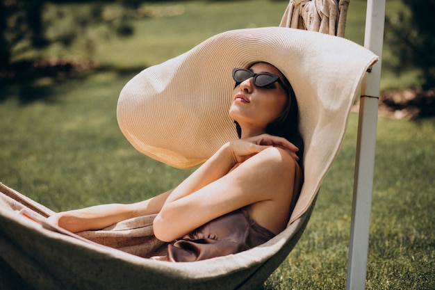 Photo gratuite belle femme allongée dans un hamac portant un gros chapeau de soleil