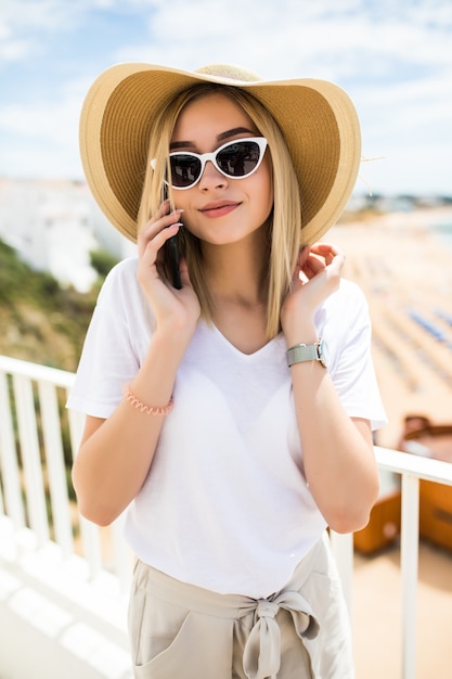 Belle femme appuyée sur la balustrade de la terrasse, se détendre et avoir un appel téléphonique