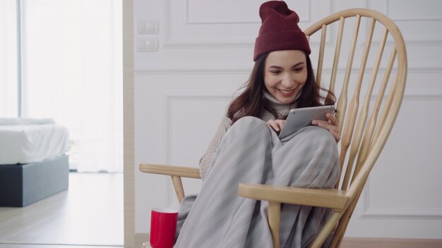 Belle femme asiatique attrayante à l&#39;aide d&#39;une tablette pour envoyer des SMS et lire assis sur une chaise