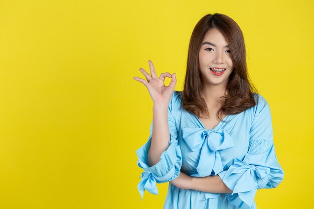 Belle femme asiatique avec un geste okey sur mur jaune