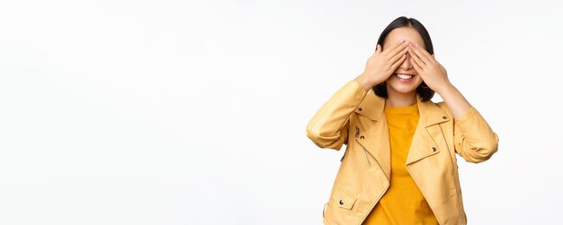 Belle femme asiatique heureuse ferme les yeux bandés en attendant la surprise et souriante anticipant les cadeaux en vacances debout sur fond blanc