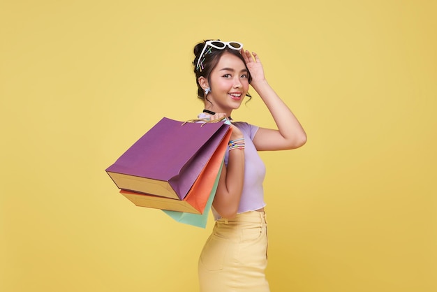 Photo gratuite une belle femme asiatique heureuse portant des sacs d'achat colorés isolés sur un fond de studio jaune