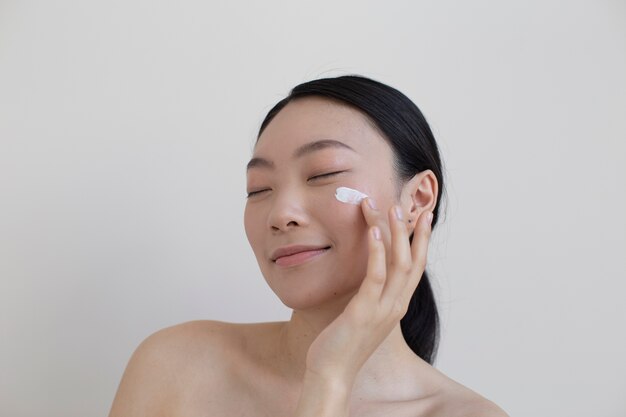 Belle femme asiatique posant avec de la crème pour le visage