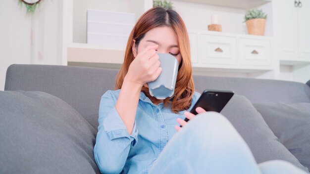 belle femme asiatique souriante attrayante à l&#39;aide de smartphone tenant une tasse de café