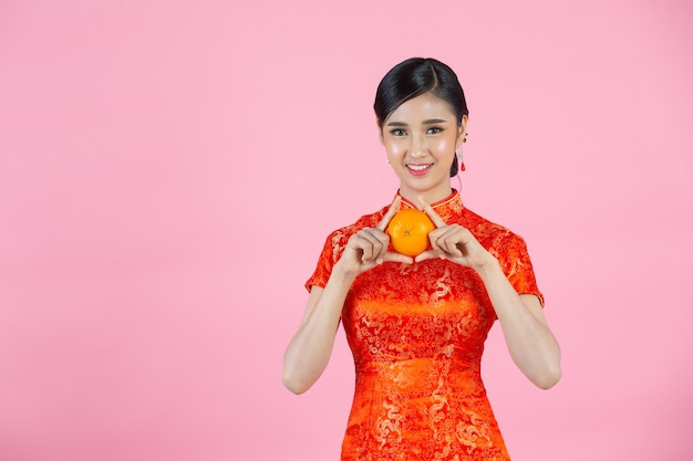 Belle femme asiatique sourire heureux et tenant des oranges fraîches au nouvel an chinois sur fond rose.