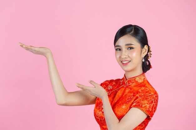 Belle femme asiatique sourire heureux et vous montrer quelque chose au nouvel an chinois sur fond rose.