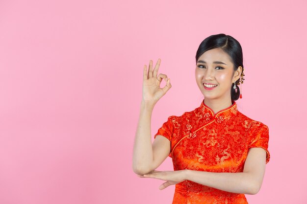 Belle femme asiatique sourire heureux et vous montrer quelque chose au nouvel an chinois sur fond rose.