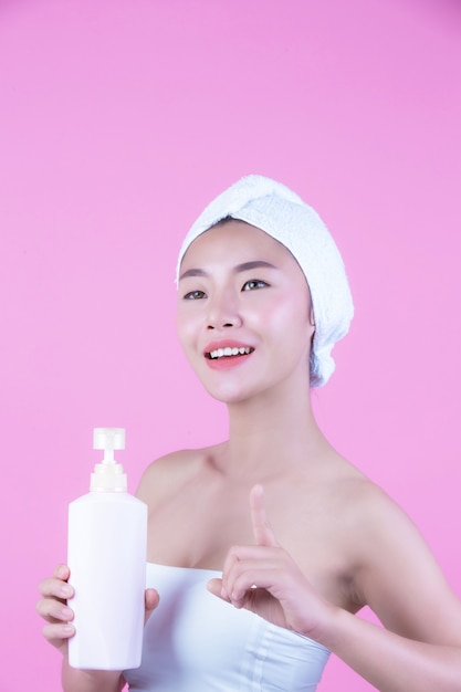 Belle femme asiatique tenant une bouteille de produit sur un fond rose.