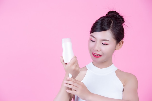 Belle femme asiatique tenant une bouteille de produit sur un fond rose.