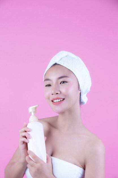 Belle femme asiatique tenant une bouteille de produit sur un fond rose.