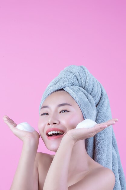 Belle femme en Asie se lave le visage sur fond rose.