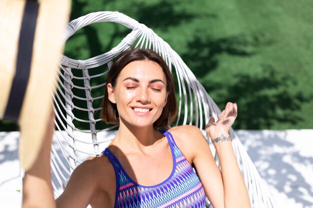 Belle femme assise sur une chaise d'arrière-cour à une journée ensoleillée d'été, profitant d'un temps chaud incroyable, attrapant les rayons du soleil