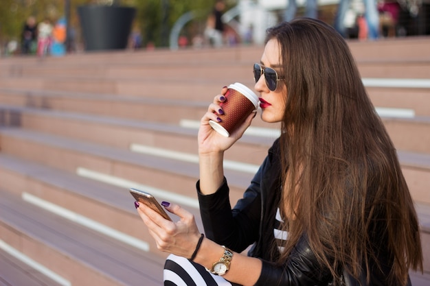 Belle femme assise sur les escaliers et regardant le téléphone portable.