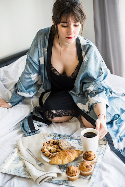 Photo gratuite belle femme assise sur le lit, prenant son petit déjeuner