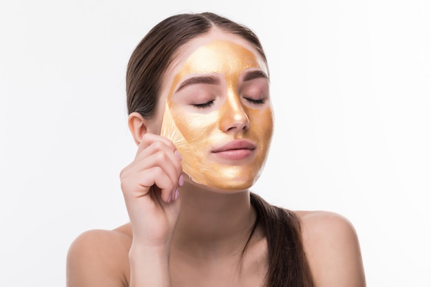 Belle femme au visage tactile cosmétique peau dorée isolé sur mur blanc. Soins et soins de beauté