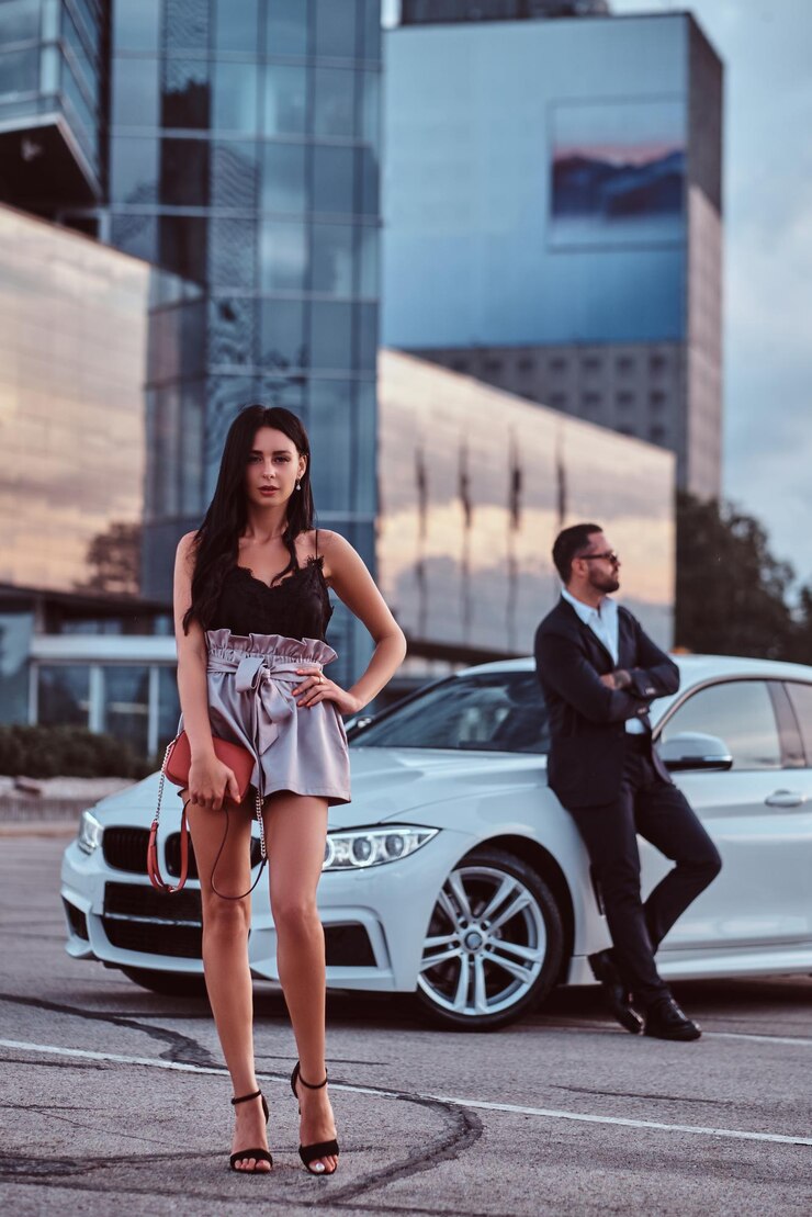 Photo gratuit belle femme bien habillée et homme brutal en costume près d'une voiture de luxe à l'extérieur contre un paysage urbain.