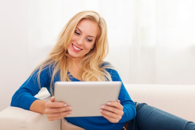Belle femme blonde à l'aide de tablette numérique sur canapé