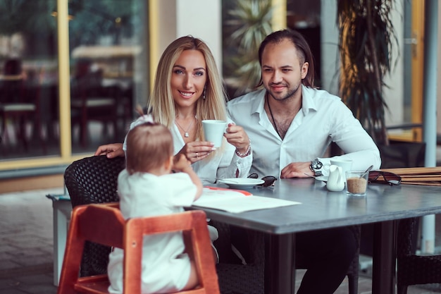 Belle femme blonde et beau mâle pendant le temps avec leur petite fille dans un café en plein air. Concept de famille et de personnes.