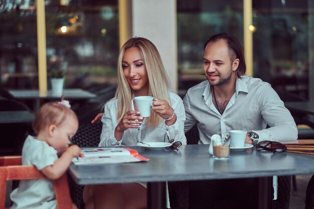 Belle femme blonde et beau mâle profitant de la vie de famille avec leur petite fille dans un café en plein air.