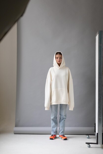 Une belle femme blonde dans un sweat à capuche blanc et un jean bleu posant sur un fond gris