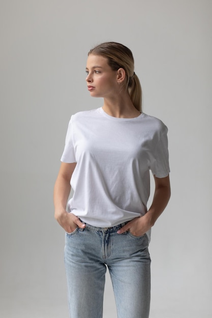 Une belle femme blonde dans un t-shirt blanc et un jean bleu posant sur un fond blanc