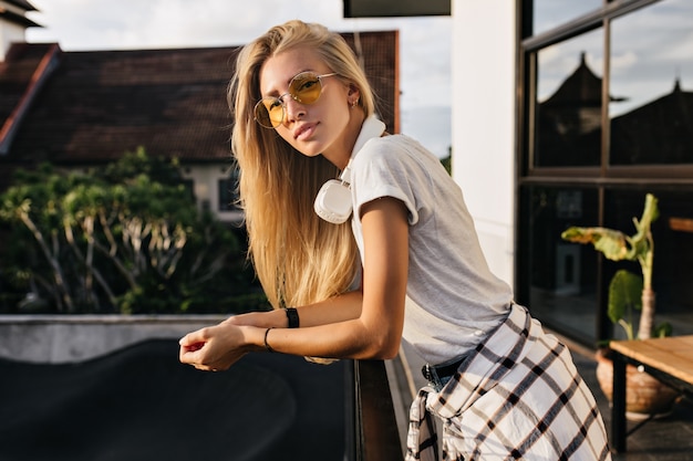 Belle femme blonde dans des vêtements à la mode posant avec l'expression du visage intéressé en journée d'été.