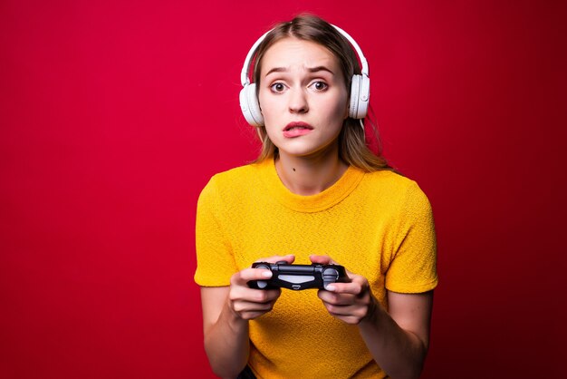 Belle femme blonde avec joystick et écouteurs sur mur rouge