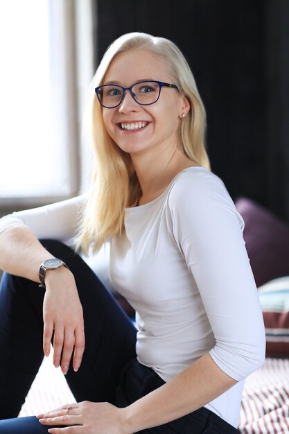 Belle femme blonde avec des lunettes posant en chemise blanche