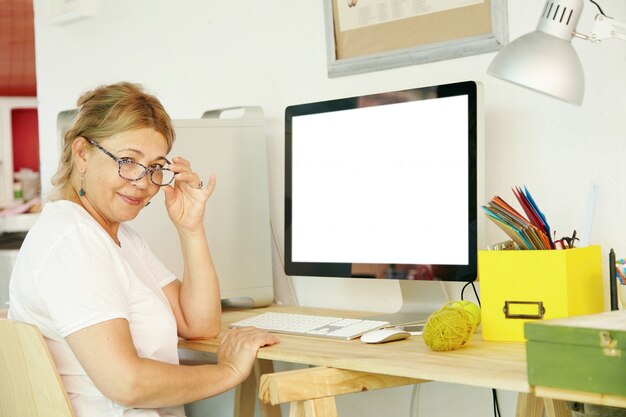 Belle femme blonde mature retraité à lunettes assis devant l'ordinateur