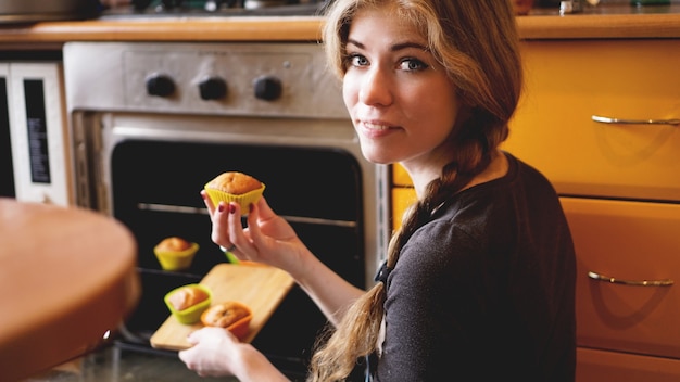 Belle femme blonde montrant des muffins dans une cuisine. concept de cuisine et de maison