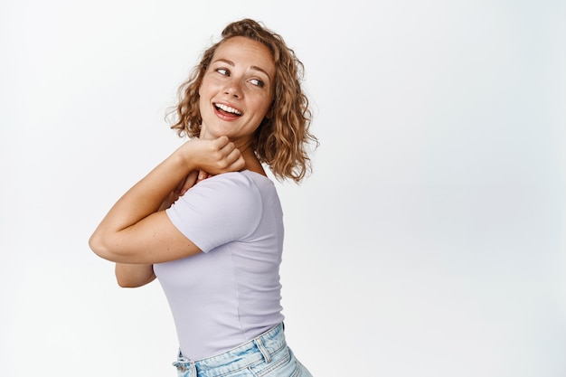 Belle femme blonde se retourne, regardant derrière son épaule et souriant, lisant l'espace de copie, debout sur blanc