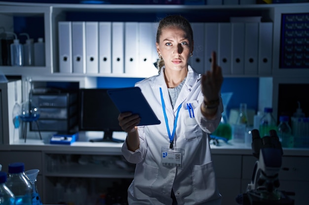 Photo gratuite belle femme blonde travaillant dans un laboratoire scientifique tard dans la nuit montrant un majeur impoli et grossier expression de baise