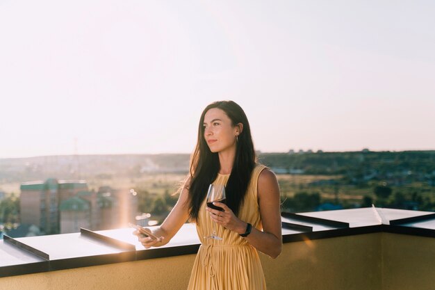 Belle femme boit du vin sur le toit au soleil