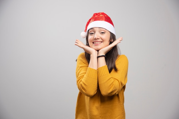 Belle femme en bonnet de Noel se sentant heureuse sur un mur gris.