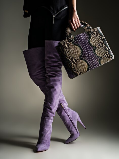 Belle femme en bottes hautes violettes. Fille à la mode tient élégant sac en cuir violet. Concept élégant glamour. Art. Modèle marche après le shopping.