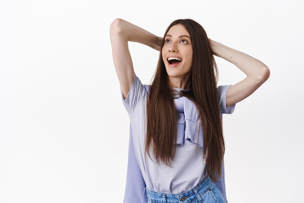 Belle femme brune à l'air joyeuse dans le coin supérieur gauche, se reposant les mains derrière la tête et riant, se relaxant, debout sur un mur blanc