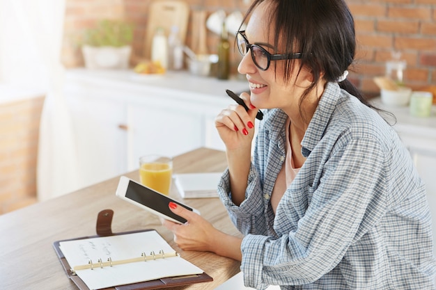 Belle femme brune à la maison, utilise une tablette moderne pour établir des contacts avec des amis ou des parents