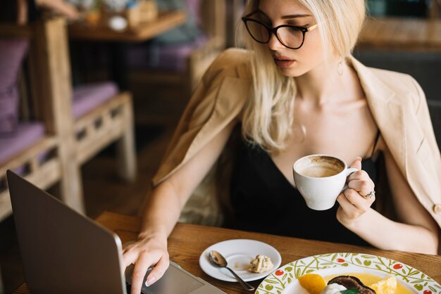 Belle femme buvant du café dans le café tout en utilisant un ordinateur portable