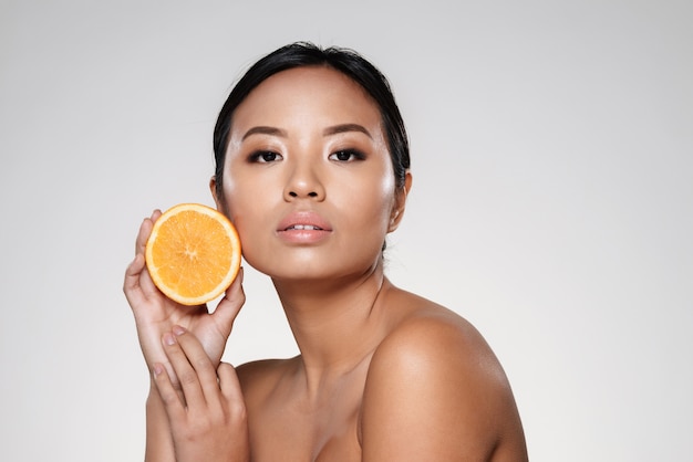 Belle femme calme montrant une tranche d'orange et regardant la caméra