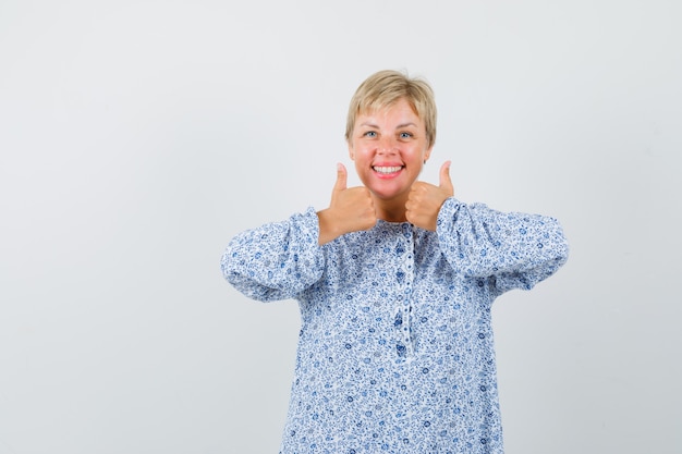 Belle femme en chemisier à motifs montrant le pouce vers le haut tout en souriant et en regardant jolly, vue de face.